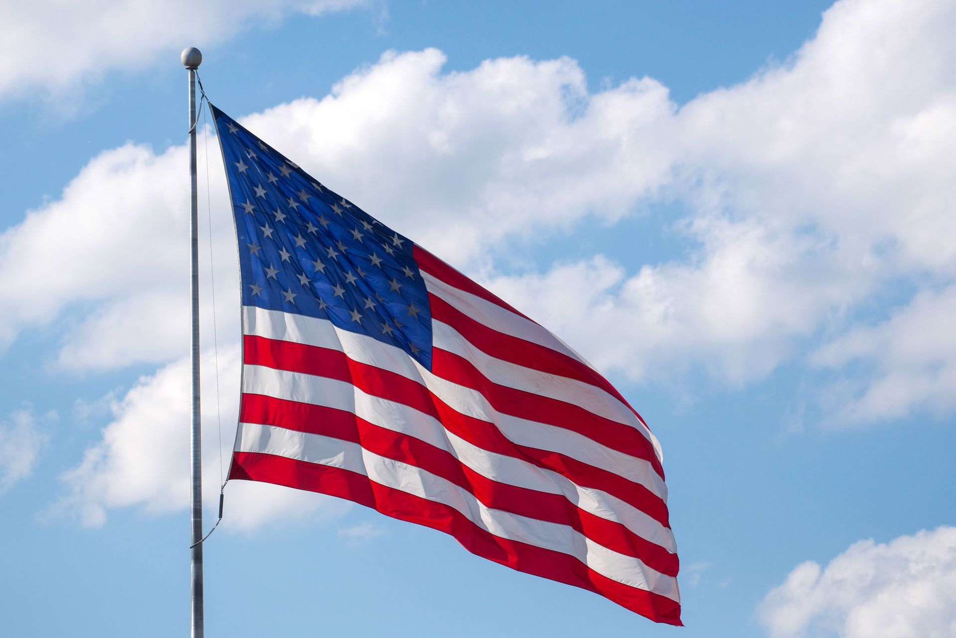 American flag waving against a blue sky with clouds
