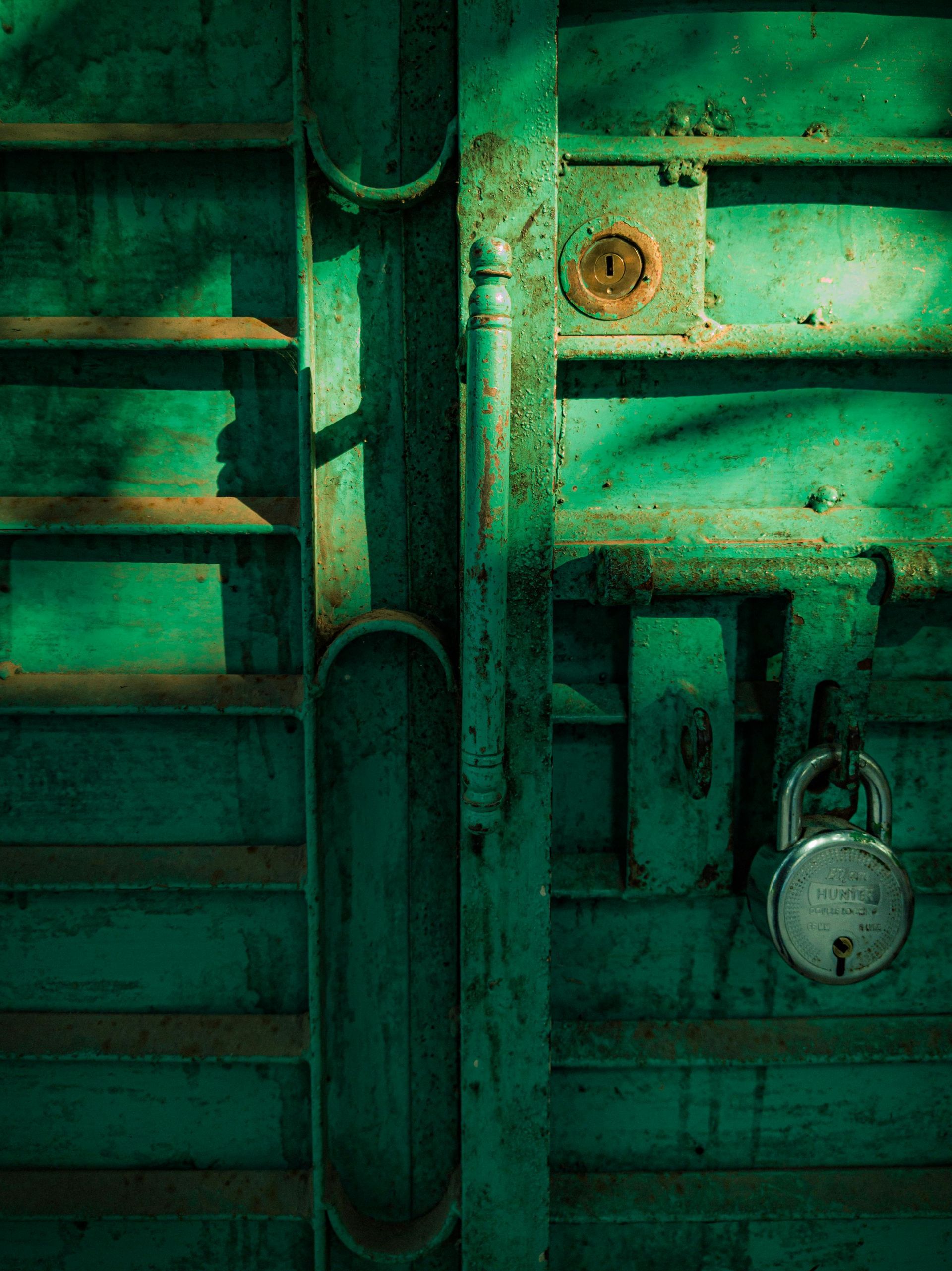 Green weathered metal door with a padlock and rusted latch.