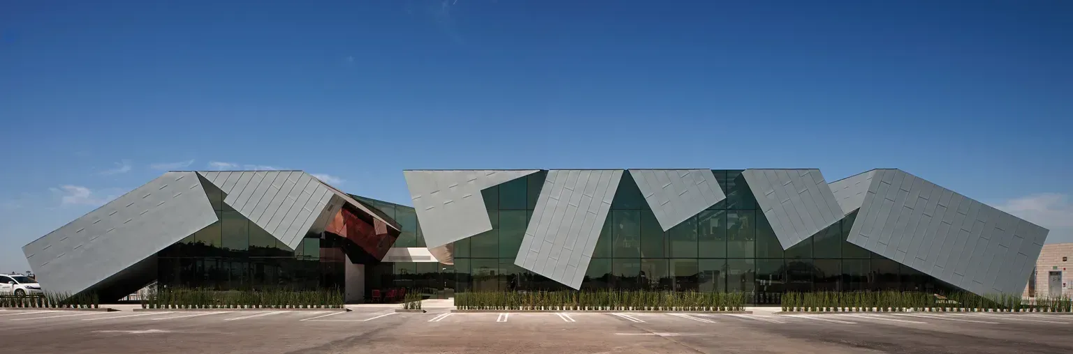 Modern building with angular green and gray geometric panels under a blue sky