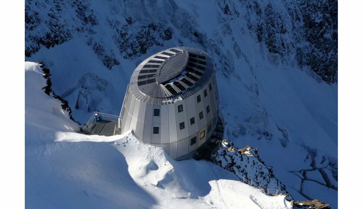 Snow-covered mountain hut with a rounded roof on a steep snowy slope