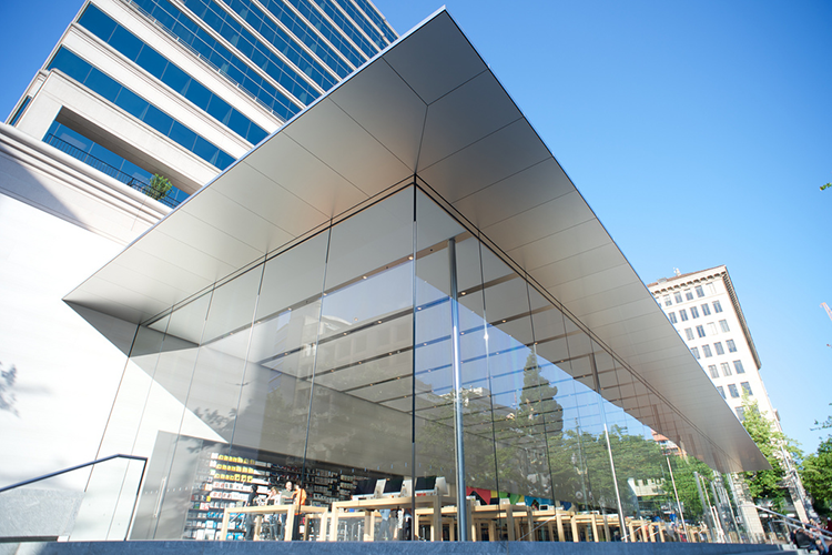 Modern glass building entrance with a large cantilevered roof and blue sky