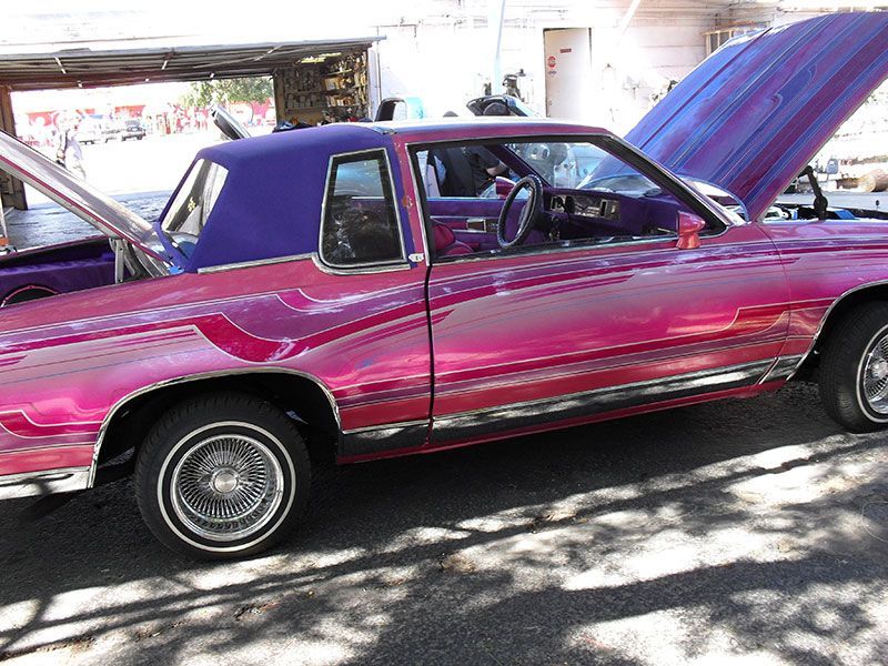 Bright pink classic car parked outdoors with its hood open and another car beside it