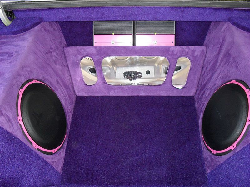Purple-carpeted car audio trunk with two large speakers and a center amplifier panel