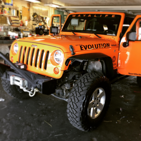 Orange Jeep Wrangler with off-road tires and 'EVOLUTION' lettering in a garage.