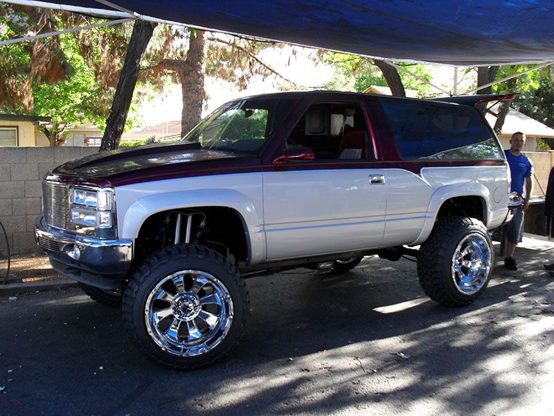 Lifted silver and black SUV parked outdoors under trees, with chrome wheels and a person standing nearby.