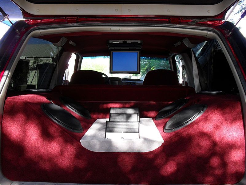 Red car trunk with red carpet interior and a small monitor mounted at the back seat.