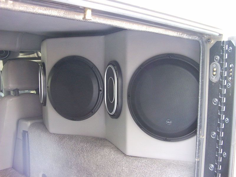 Car audio setup with two large subwoofers and a small speaker in a gray enclosure