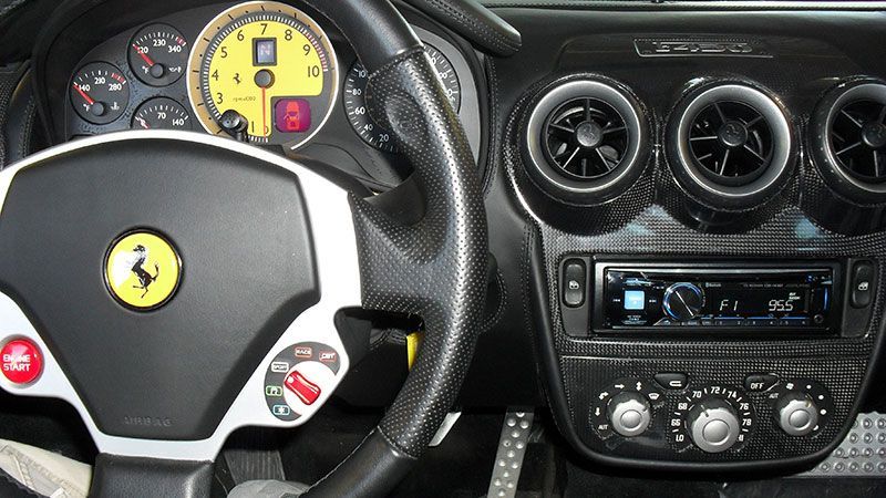 Ferrari car interior with steering wheel, dashboard gauges, air vents, and center console