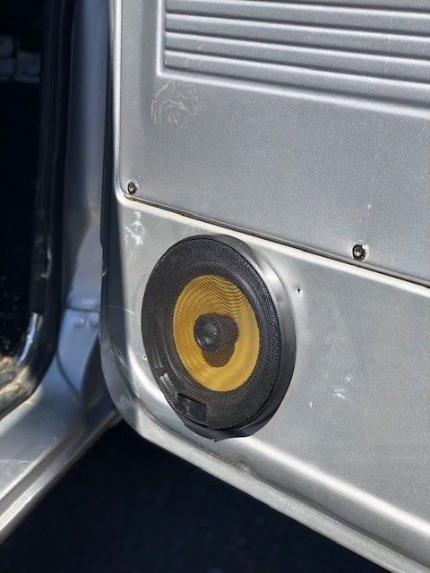 Yellow speaker mounted in a silver vehicle door panel near the open door.