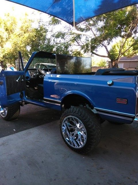 Blue lifted pickup truck with chrome wheels parked outdoors under a canopy.