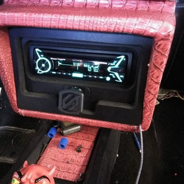 Custom pink car dashboard with a glowing digital stereo and exposed wiring in a dark interior