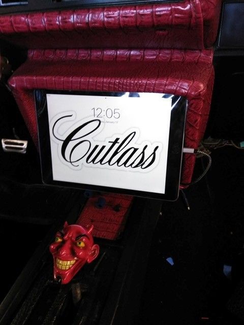 Custom car interior with red upholstery, a screen reading “Cutlass,” and a small red dragon figurine on the floor.