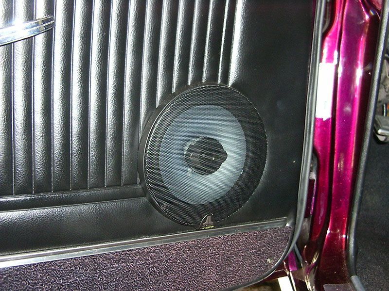 Black speaker mounted in a car door panel with magenta trim nearby