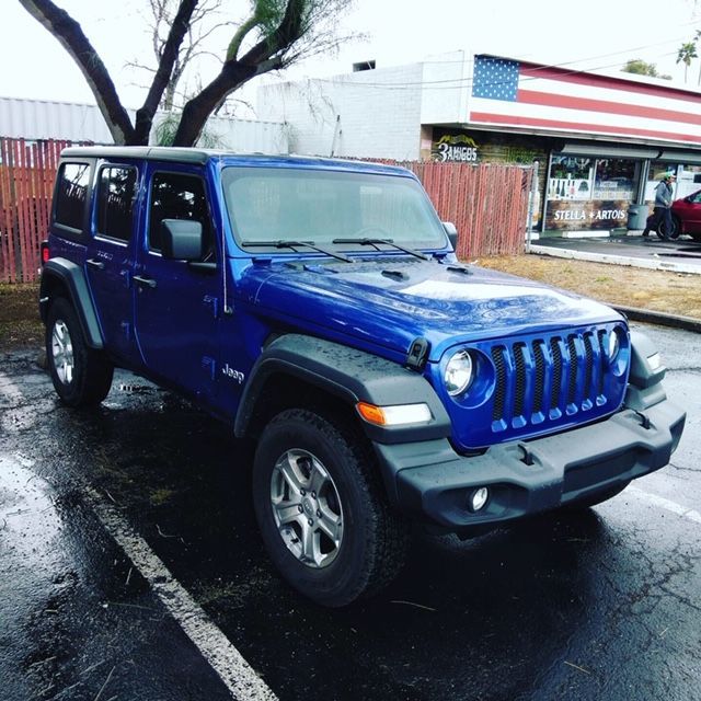 Blue Jeep Wrangler parked on a wet street in front of a storefront