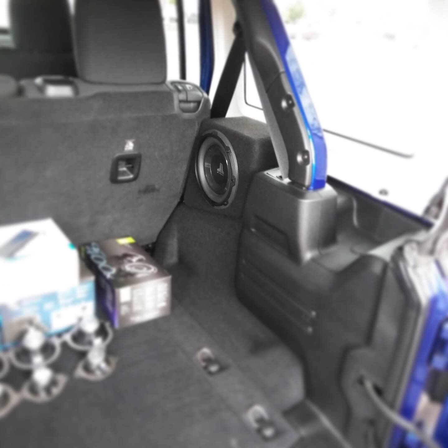 Car trunk interior with a subwoofer, boxes, and folded seat in a blue vehicle