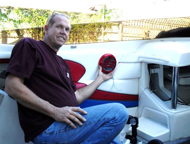 Man seated beside a white vehicle, holding up a red circular part near the rear wheel