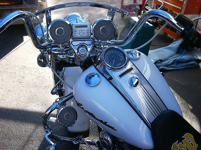 Chrome motorcycle dashboard and handlebars with speakers and a clear windshield, parked outdoors