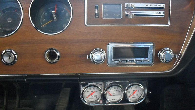 Vintage car dashboard with wood paneling, radio, gauges, and three auxiliary dials below