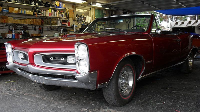 Red Pontiac GTO convertible in a garage, viewed from the front-left side.