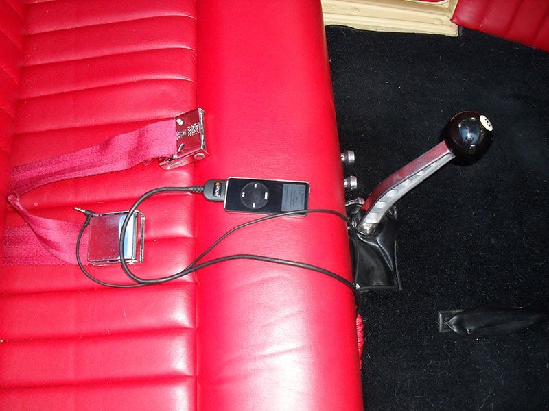 Red car seat with a seatbelt buckle, loose wires, and a gear shift lever beside it.