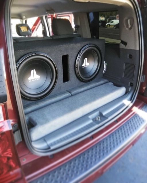Red SUV trunk with a large black speaker box and two subwoofers inside.