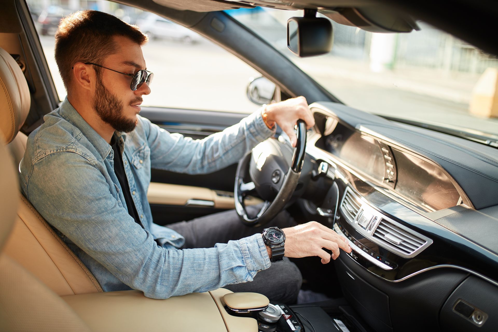 Man driving a car, wearing sunglasses and a blue shirt, hand on the wheel in the driver’s seat