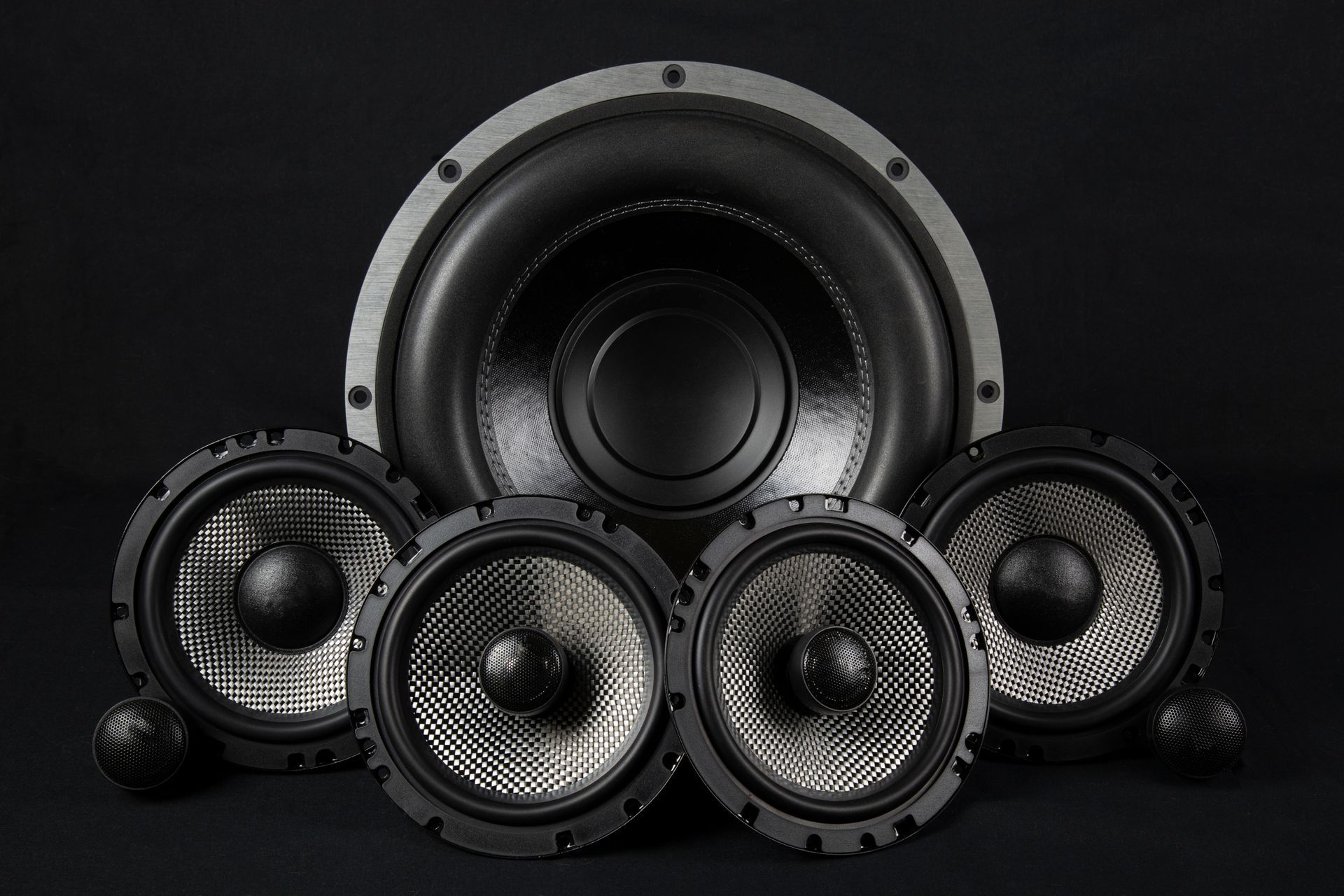 Black speaker setup with one large subwoofer and four smaller speakers on a dark background