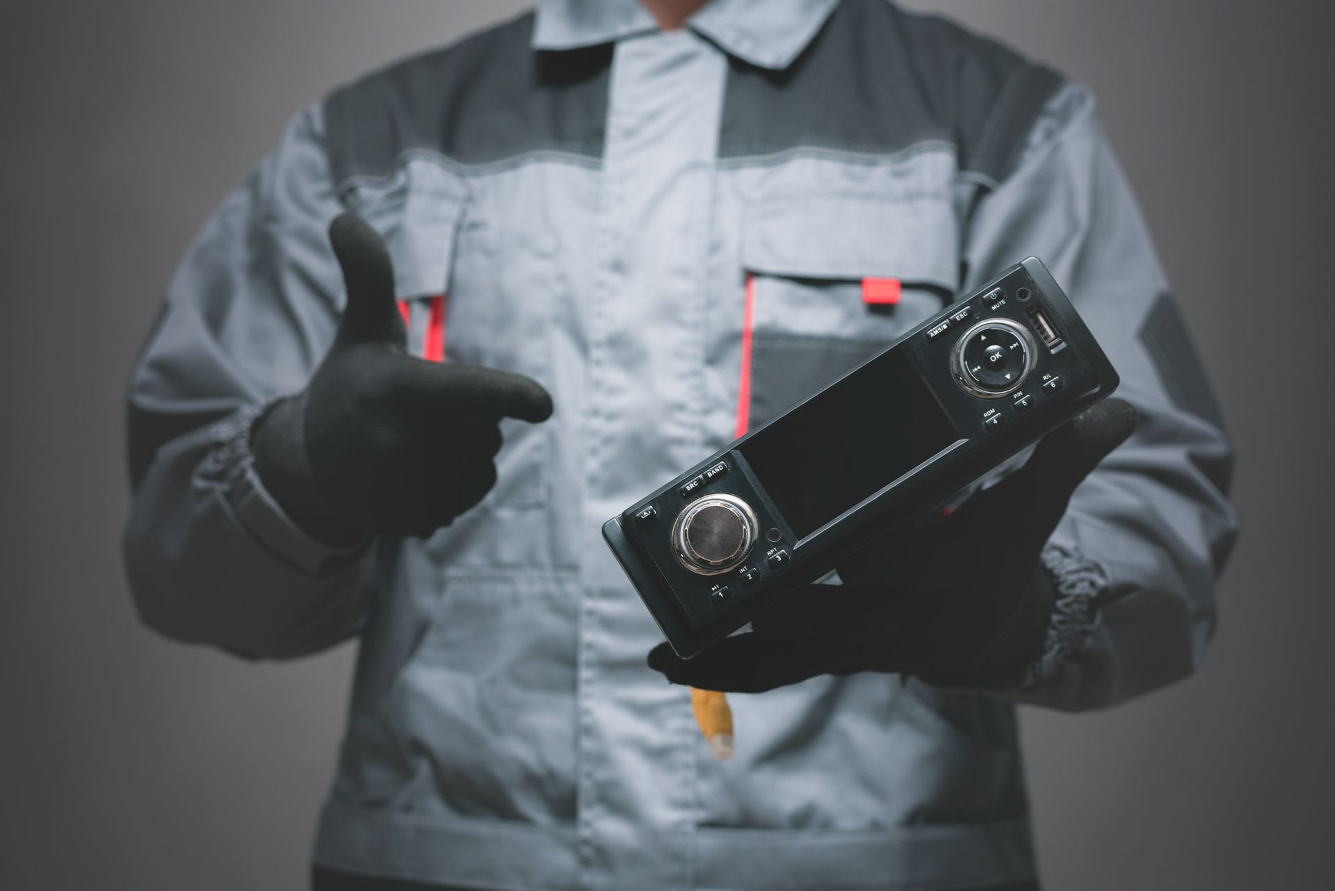 Technician holding a car stereo unit and giving a thumbs-up.