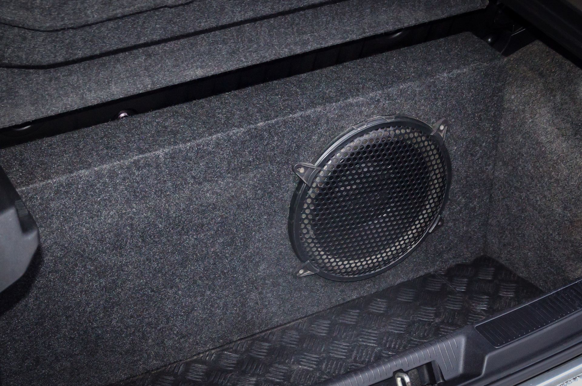 Black car trunk speaker enclosure with a round speaker grille and textured carpeting