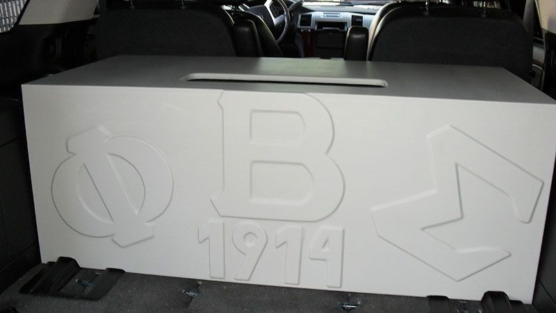 White box with embossed Greek letters Phi, Beta, Sigma and “1914” in a car trunk.