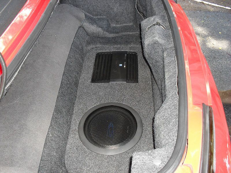 Car trunk compartment with two black speakers in gray carpeting and red body panels