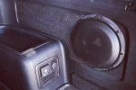 Black speaker mounted on a car interior panel beside a small control unit.