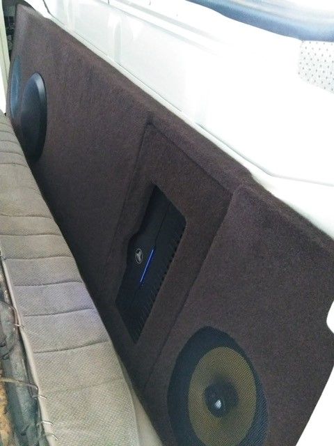 Brown upholstered bench seat with built-in round speakers and a central control panel against a light wall