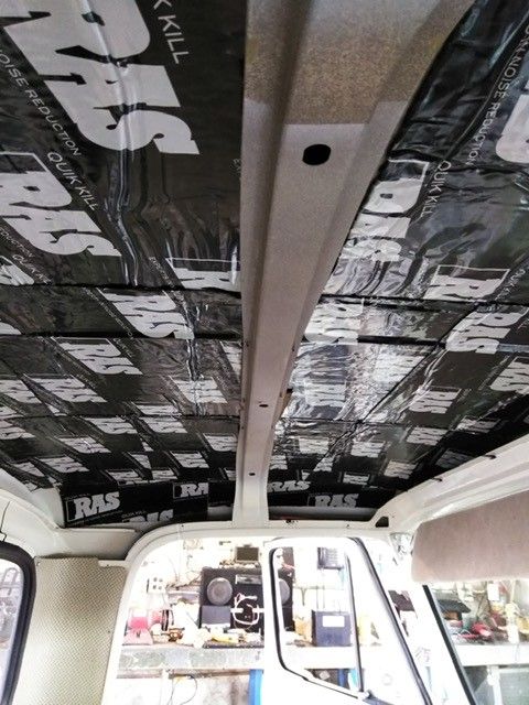 Van interior with black soundproofing insulation on the ceiling and walls, viewed from the back.