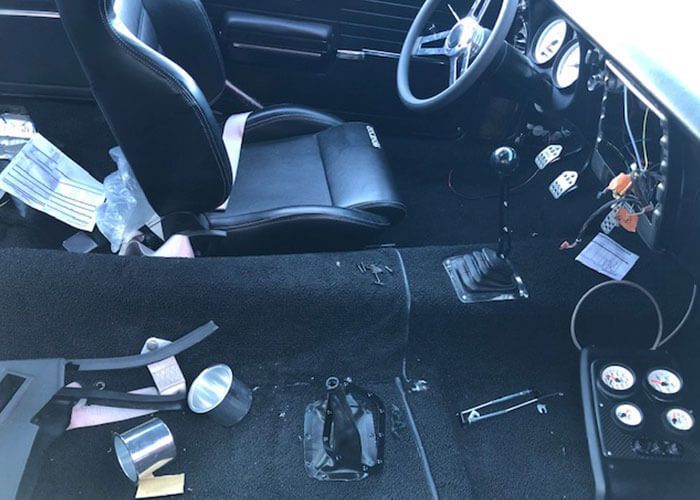 Inside a car’s front interior, with scattered tools, papers, and a detached seat or console panel on the floor