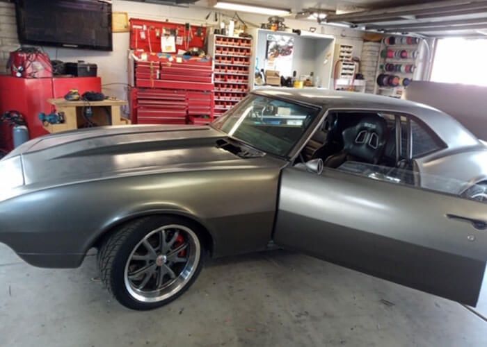 Silver classic muscle car in a garage, door open, with red tool cabinets in the background