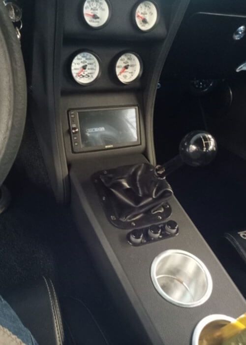Car interior with aftermarket gauges, a dashboard screen, and a manual gear shifter.