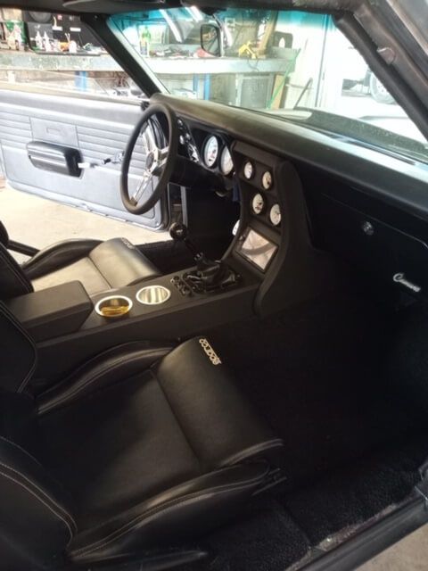 Classic car interior with black seats, wood-trim dashboard, and manual steering wheel