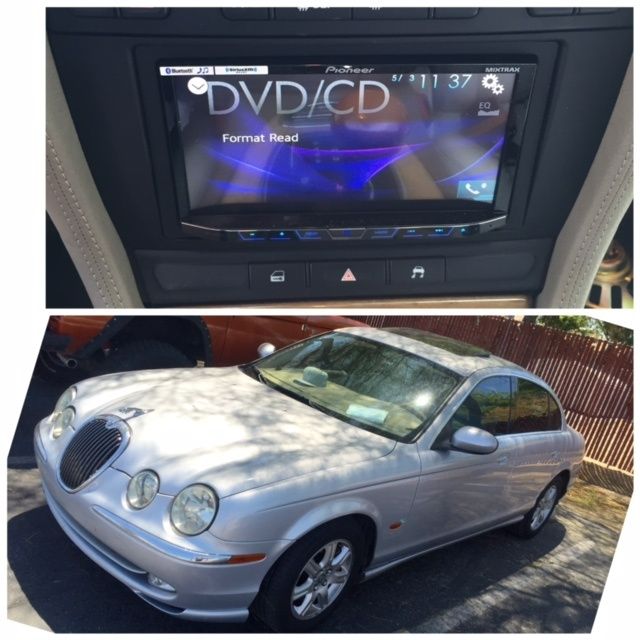 Car stereo screen above a silver Jaguar sedan parked in a driveway