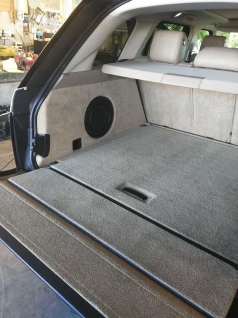 Car trunk with folded rear seats and gray carpeted cargo floor, showing a speaker panel on the left side.