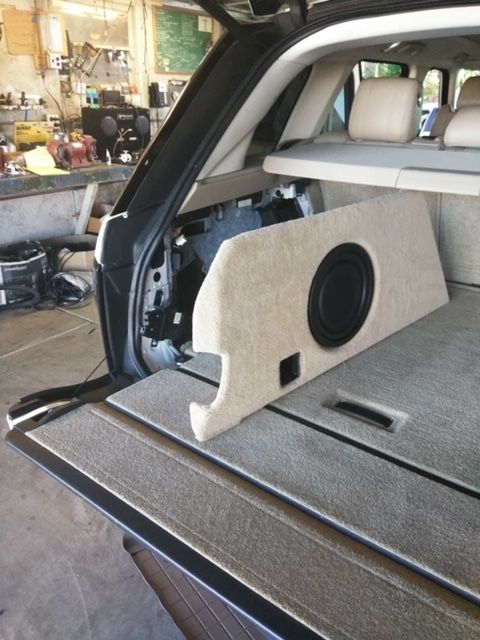 Car trunk with a custom subwoofer enclosure and beige interior panels installed.