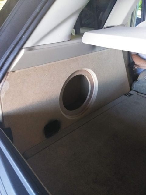 Car interior with a custom speaker enclosure and circular subwoofer opening in the rear side panel