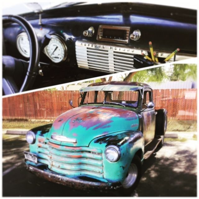 Vintage turquoise pickup truck, with dash and front view, parked outdoors by a wooden fence.