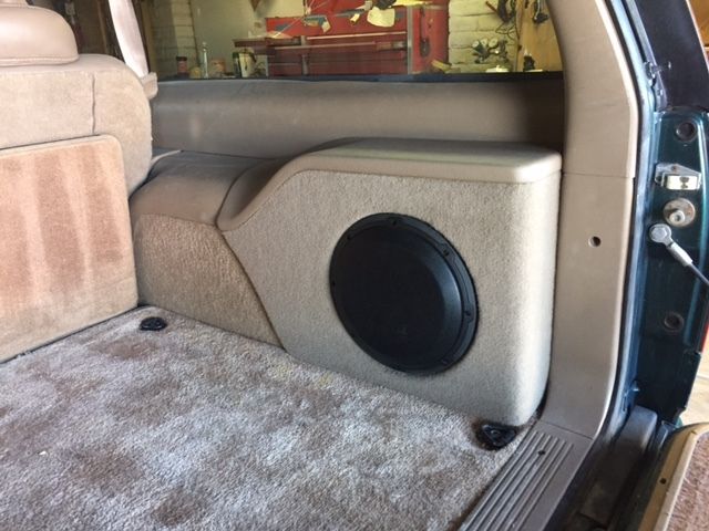 Car trunk interior with a custom beige subwoofer box and black speaker grille.