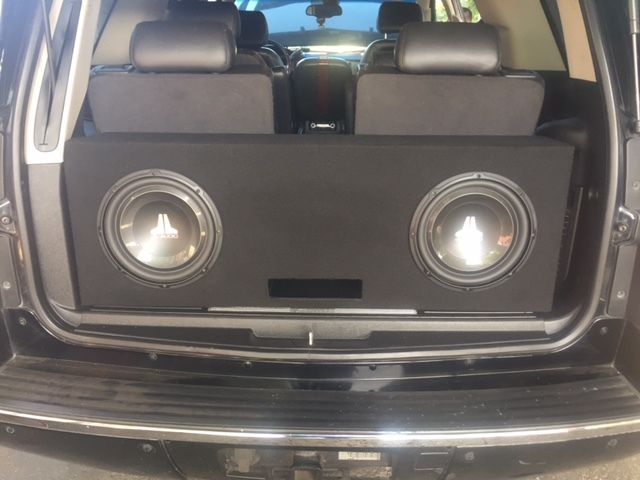 Car trunk with a custom speaker panel and two large subwoofers mounted in the back.