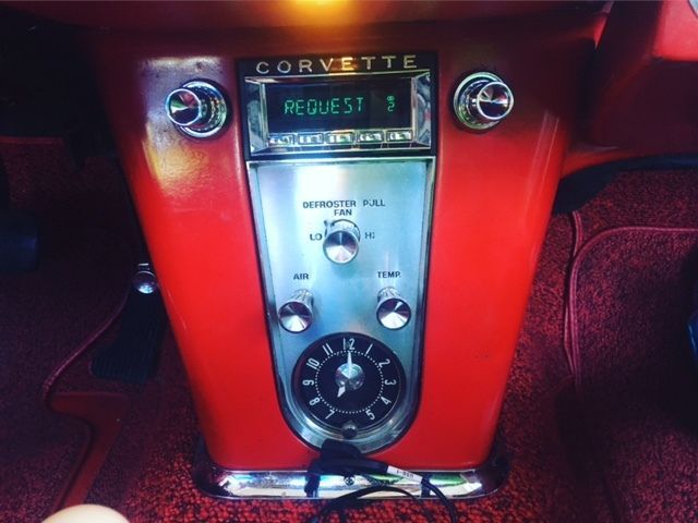 Red vintage Corvette dashboard with radio and chrome controls glowing in dim light