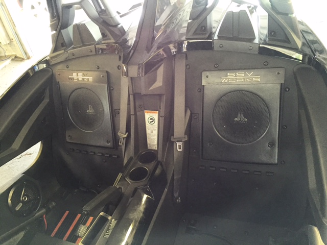 Two large black speakers mounted inside a vehicle cabin with a central console and open windows.