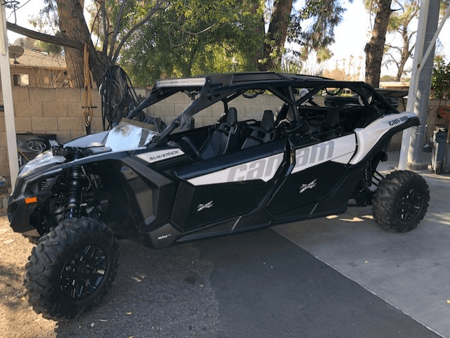 Black off-road side-by-side UTV parked outdoors on a driveway with trees in the background