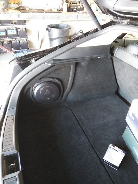 Car trunk interior with a large round speaker on the left and a small box on the floor.