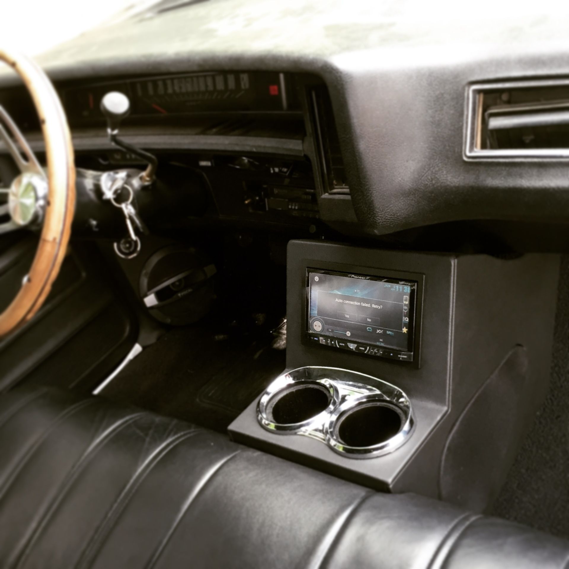 Classic car interior with black seats, wood steering wheel, and a center console touchscreen with dual cup holders